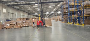 Wide warehouse view of the EOS CA2 facility showing a large storage area, loading dock, and forklift operator managing inventory flow.