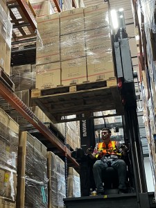 Reach forklift operator removes a pallet of outbound boxes from warehouse shelving for order fulfillment.